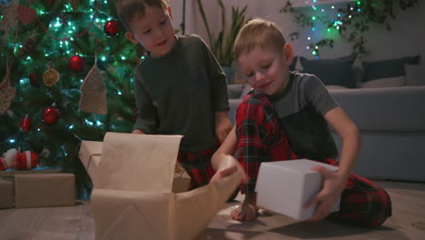 Two-boys-unpack-Christmas-presents-under-a-Christmas-tree.-Children-open-gifts.-High-quality-4k-footage
